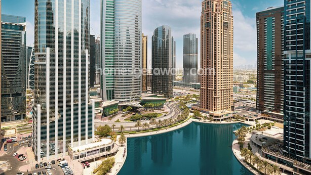 A modern urban area with high-rise buildings, a central roundabout, and a body of water. - HomesGetaway- 1BR in JLT Lake Views (Dubai)