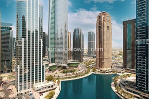 A modern urban area with high-rise buildings, a central roundabout, and a body of water. - HomesGetaway- 1BR in JLT Lake Views (Dubai)