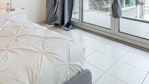 A modern bedroom with a large bed, a nightstand, and a view of the city through floor-to-ceiling windows. - HomesGetaway- 1BR in JLT Lake Views (Dubai)