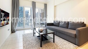 A modern living room with a glass coffee table, grey sofa, and a large window with curtains. - HomesGetaway- 1BR in JLT Lake Views (Dubai)