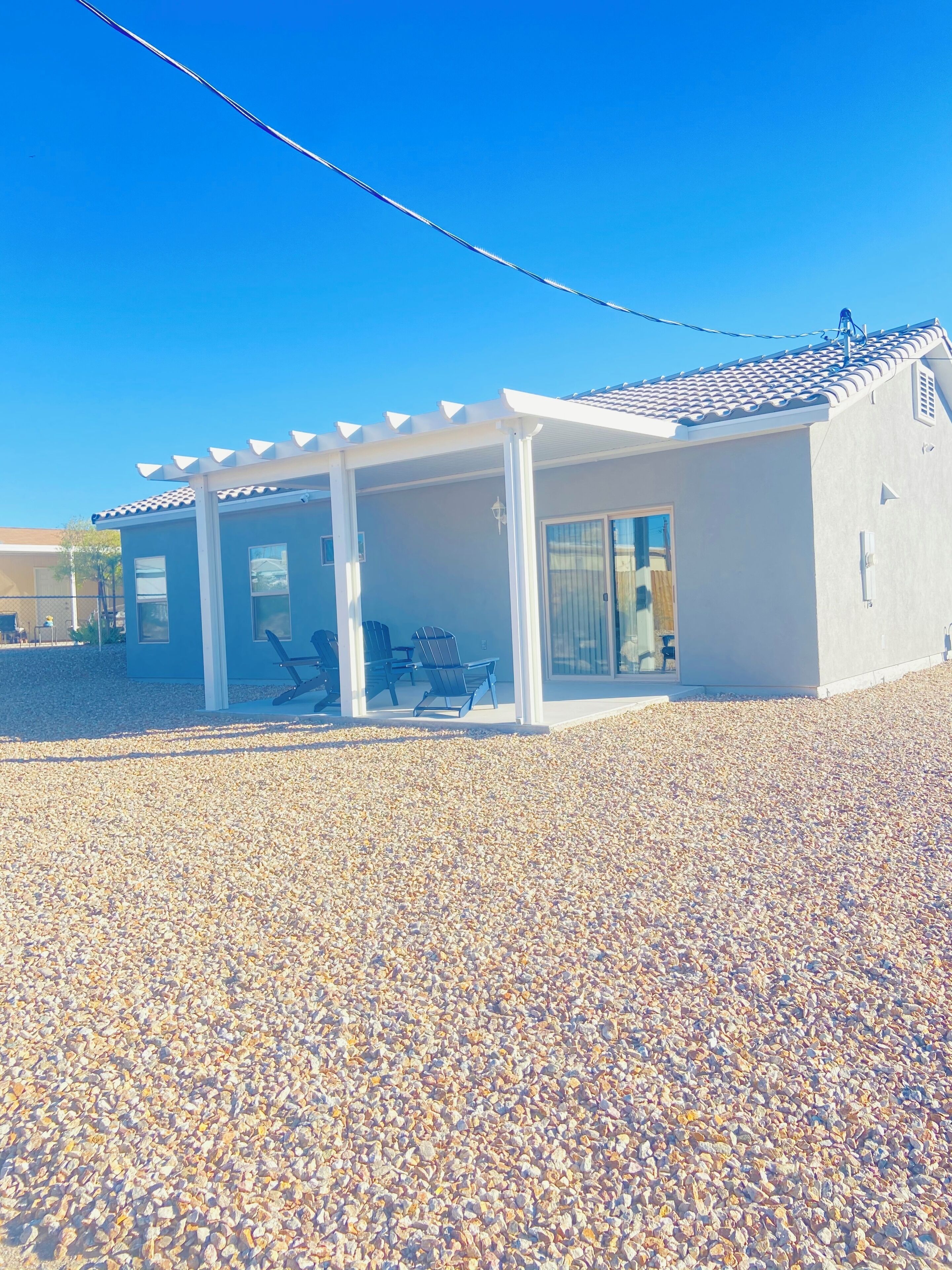 A modern house with a covered patio, a gravel driveway, and a clear blue sky.