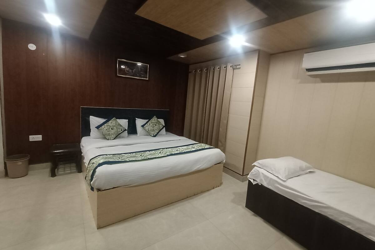 A bedroom with a large bed, a smaller bed, a TV mounted on the wall, and an air conditioning unit.
