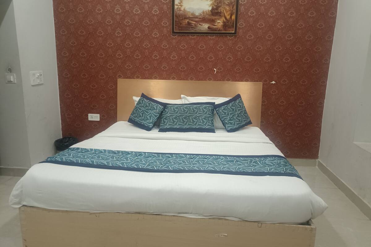 A neatly made bed with a patterned bedspread and pillows, a framed picture on the wall, and a patterned wallpaper.