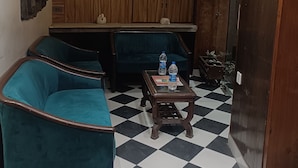 Un vestíbulo con sofás color turquesa, piso a cuadros, armarios de madera y un ventilador.