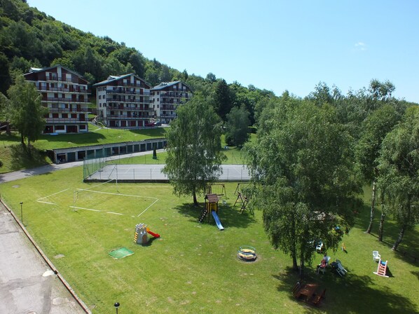 Ein Spielplatz mit Rutschen und Schaukeln, umgeben von Rasen und Bäumen.