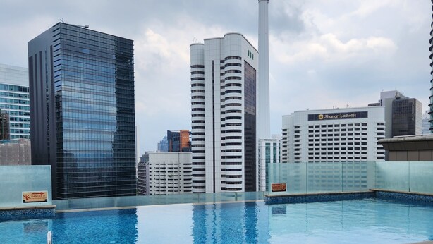 Una piscina sul tetto con lettini, circondata da edifici moderni e un'imponente torre.