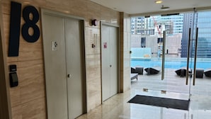 Hall d'albergo con un grande cartello con il numero 18, una reception e vista su una piscina e edifici esterni.