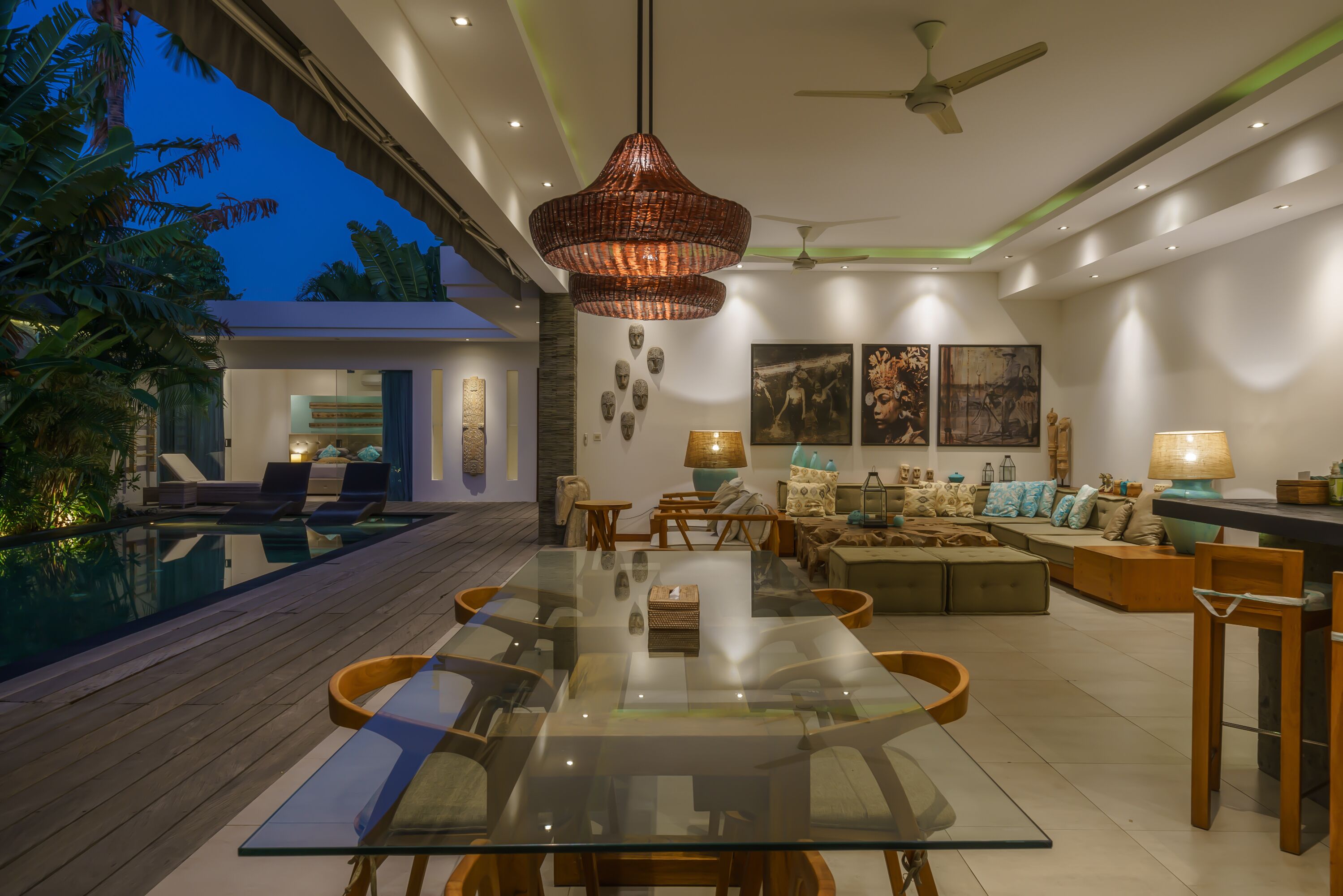 A modern living room with a glass dining table, comfortable seating, a pool, and a ceiling fan.