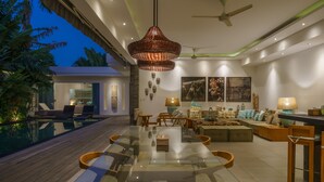 Ein modernes Wohnzimmer mit Esstisch aus Glas, bequemen Sitzmöglichkeiten, einem Pool und einem Deckenventilator.