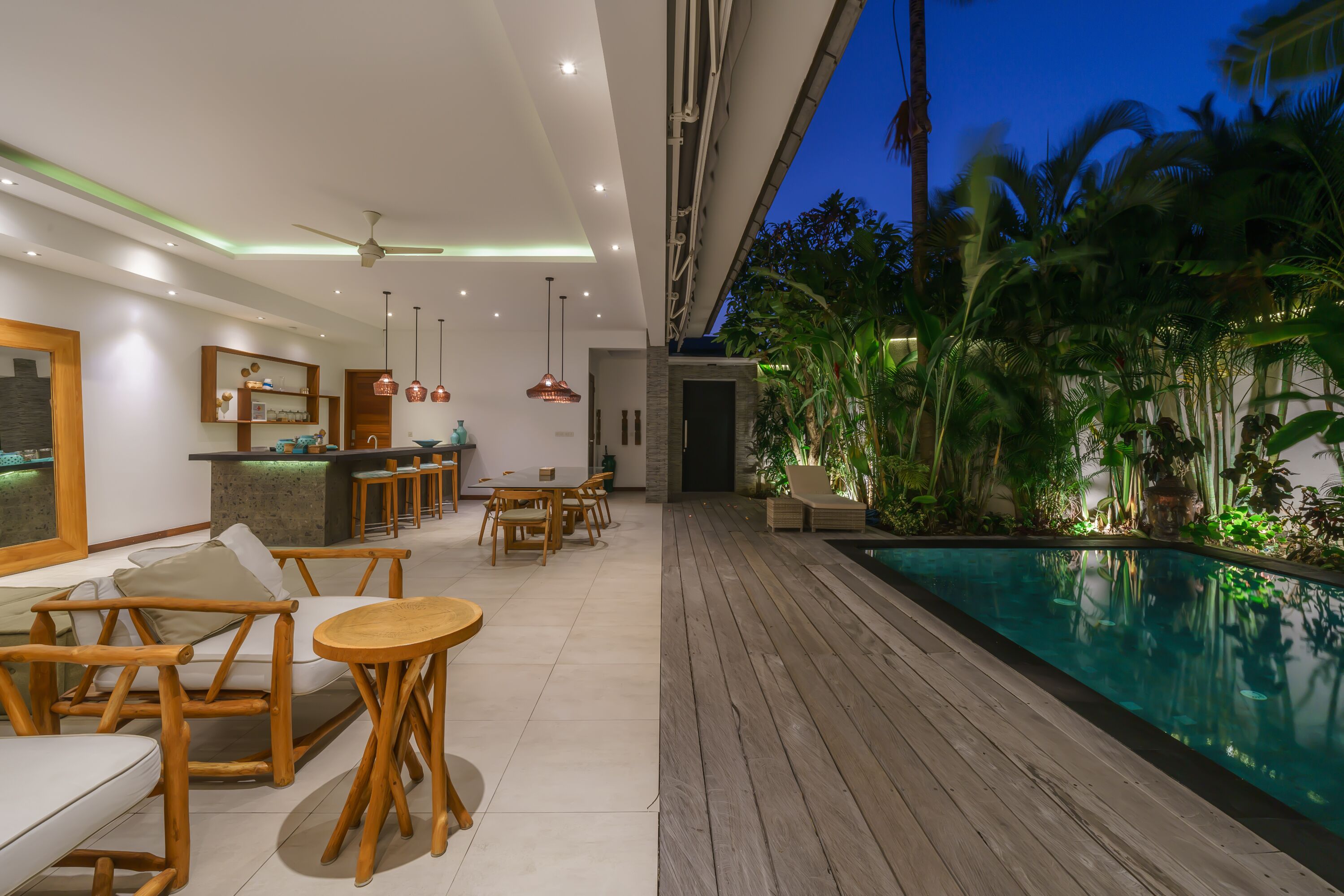 Un área de piscina interior moderna con piso de madera, asientos tipo sala de estar y una zona de bar.