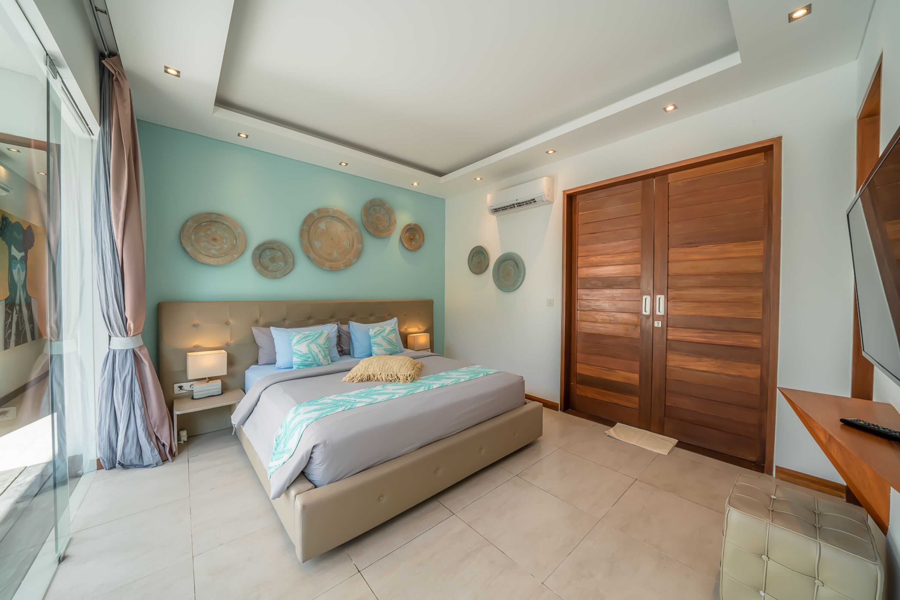 A modern bedroom with a large bed, bedside lamps, a wooden wardrobe, and decorative wall plates.