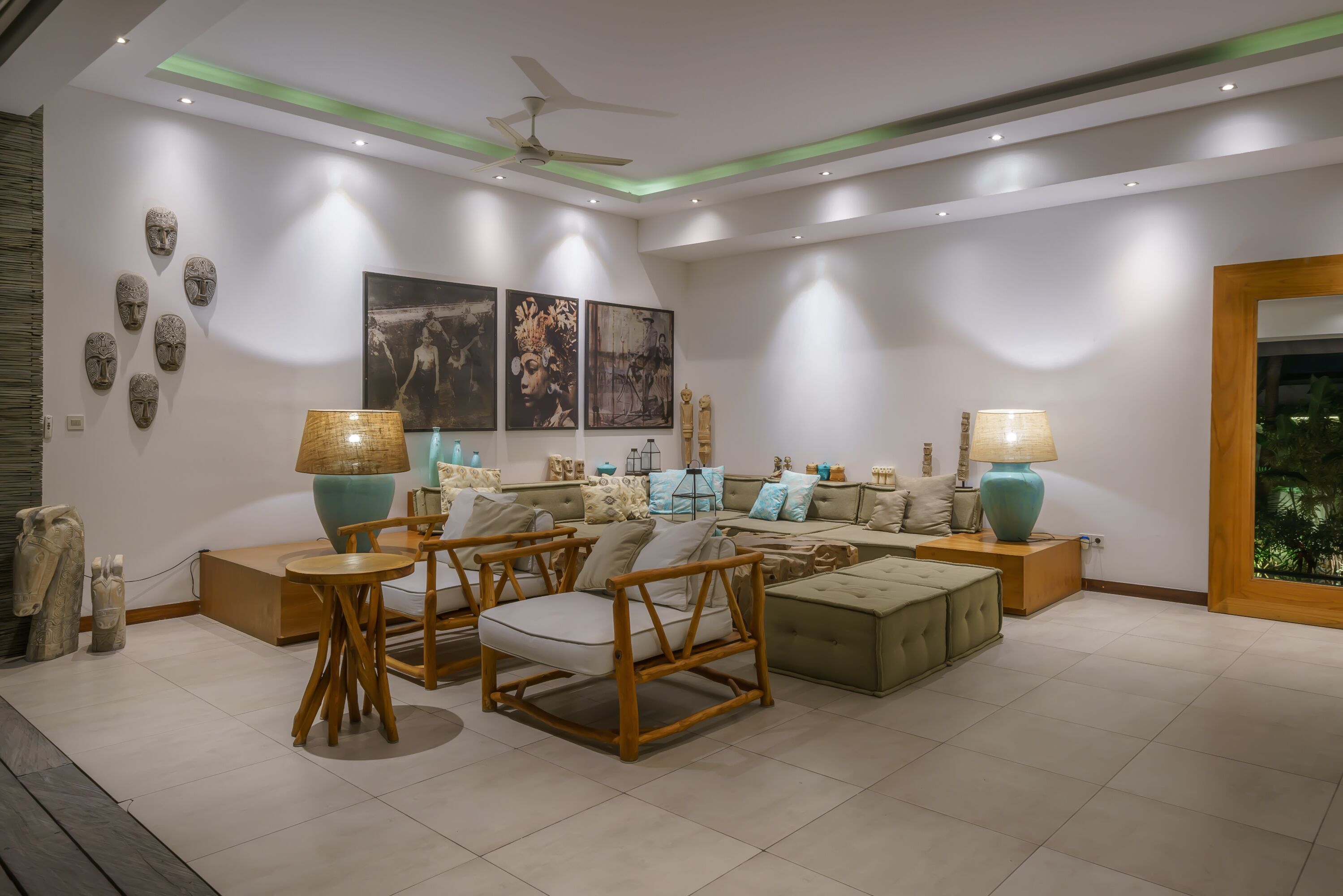 A modern living room with a sofa set, wooden chairs, and two side tables with lamps.