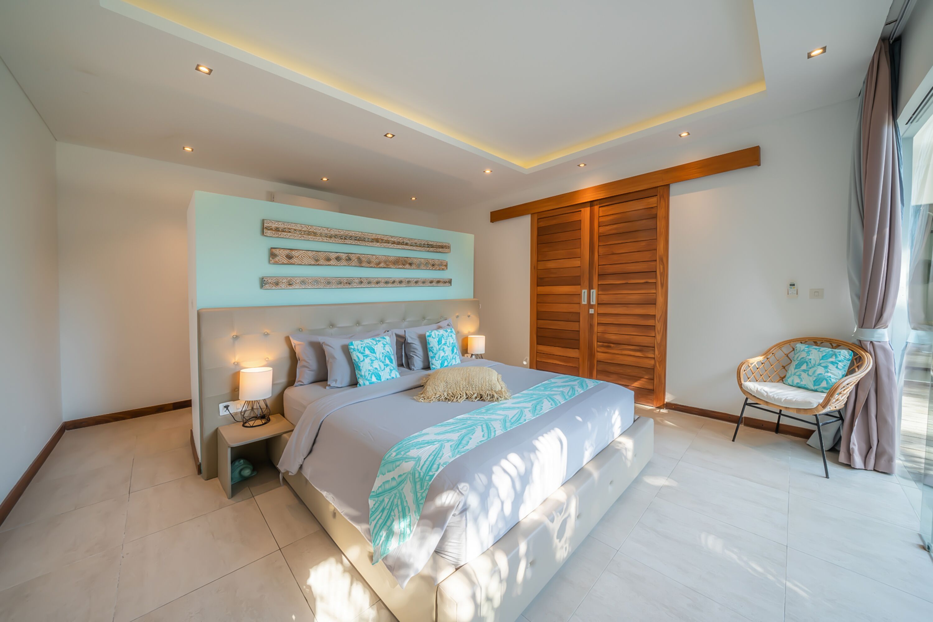 Een moderne slaapkamer met een groot bed, een houten garderobe, een rieten stoel en een kunstwerk aan de muur.