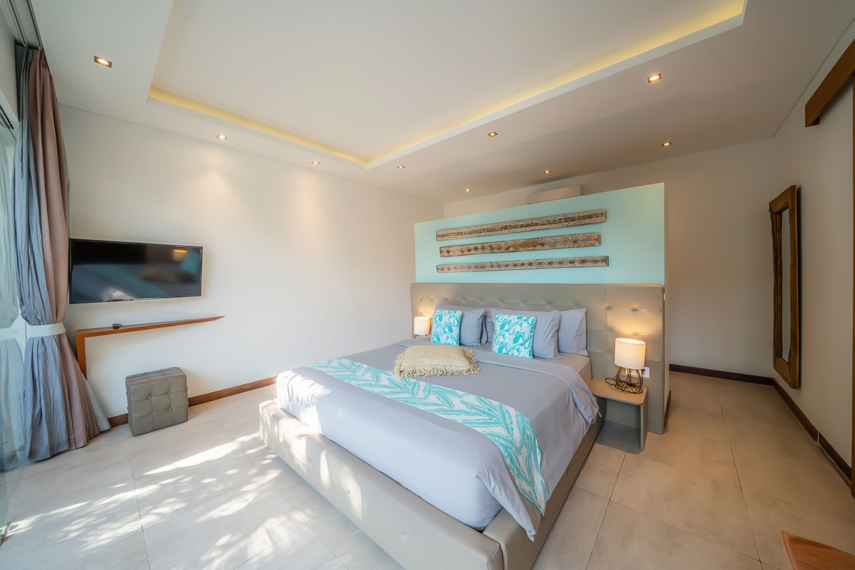 A modern bedroom with a large bed, a flat-screen TV mounted on the wall, and a ceiling with recessed lighting.