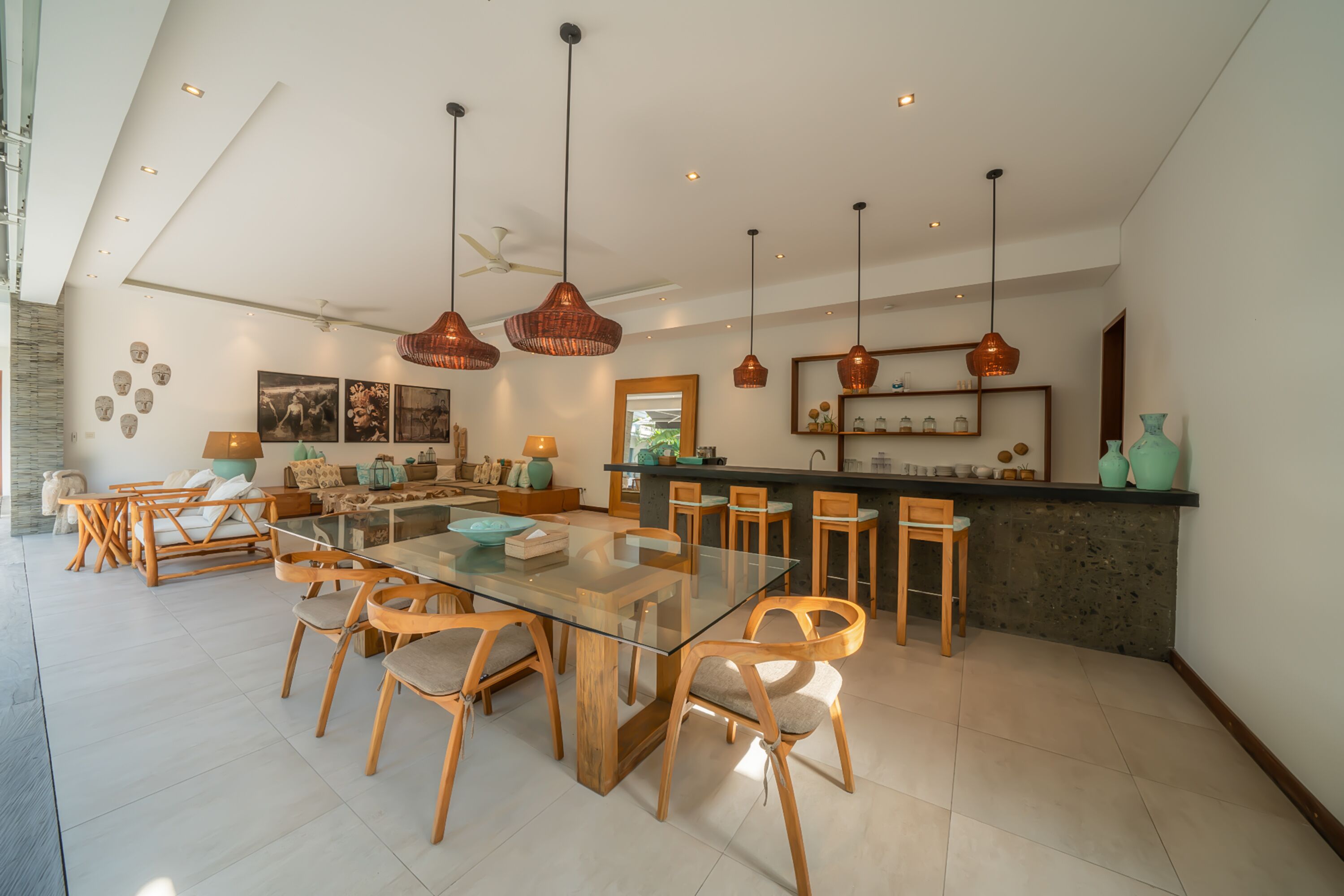 A spacious living area with a glass dining table, wooden chairs, and pendant lighting.