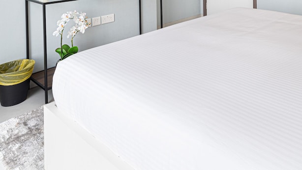 A neatly made bed in a hotel room with a small trash bin and a potted plant. - HomesGetaway- 2BR in 1Residence at Wasl1 (Dubai)