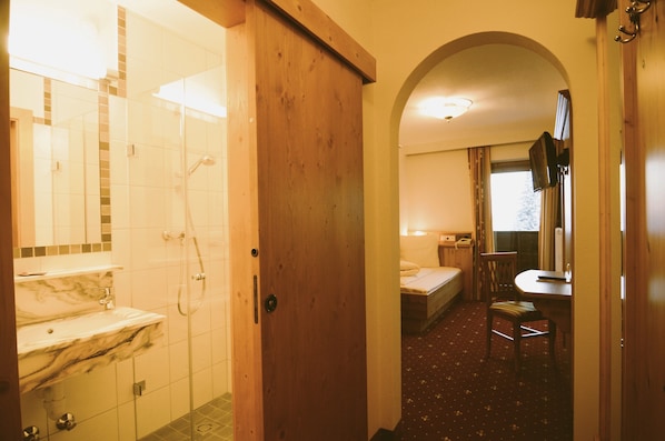 Una habitación de hotel con baño, una cama, un escritorio y una silla.