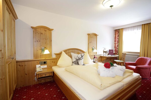 Habitación de hotel con una cama de madera, un escritorio con lámpara, una silla y una ventana con cortinas.