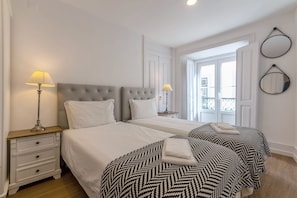 Una camera d'albergo con due letti, un comodino con cassetti, una lampada e una finestra vista.
