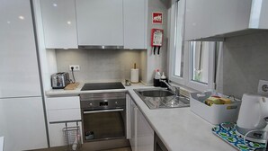 Una cocina moderna con armarios blancos, electrodomésticos de acero inoxidable, horno integrado y ventana con vistas.