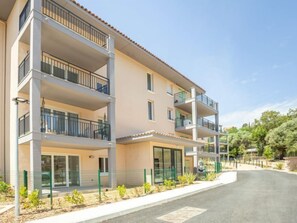Um edifício residencial com vários andares, varandas, janelas amplas e um caminho de acesso pavimentado.
