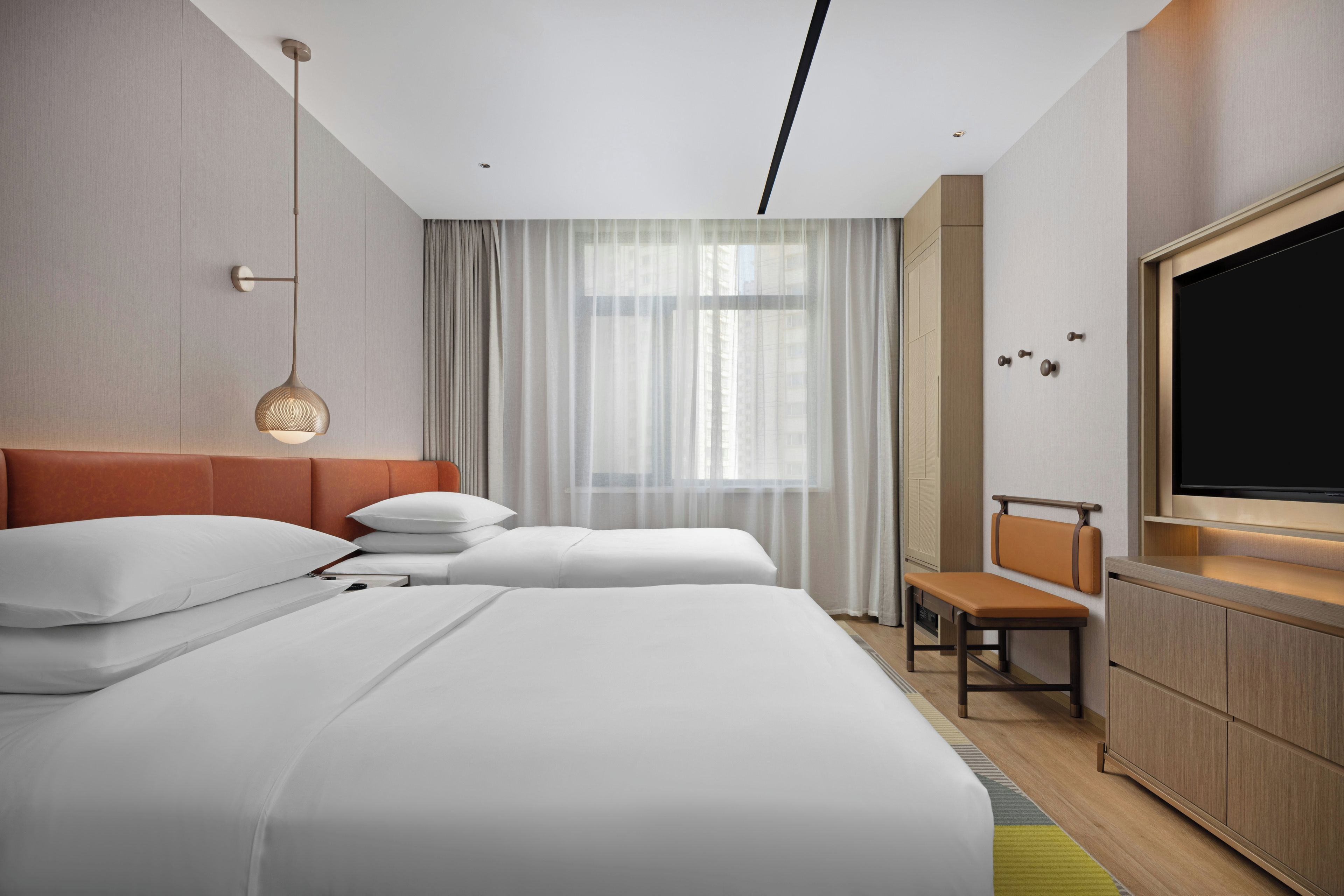 Une chambre d’hôtel avec deux lits, une télévision, un bureau et une fenêtre avec des rideaux.