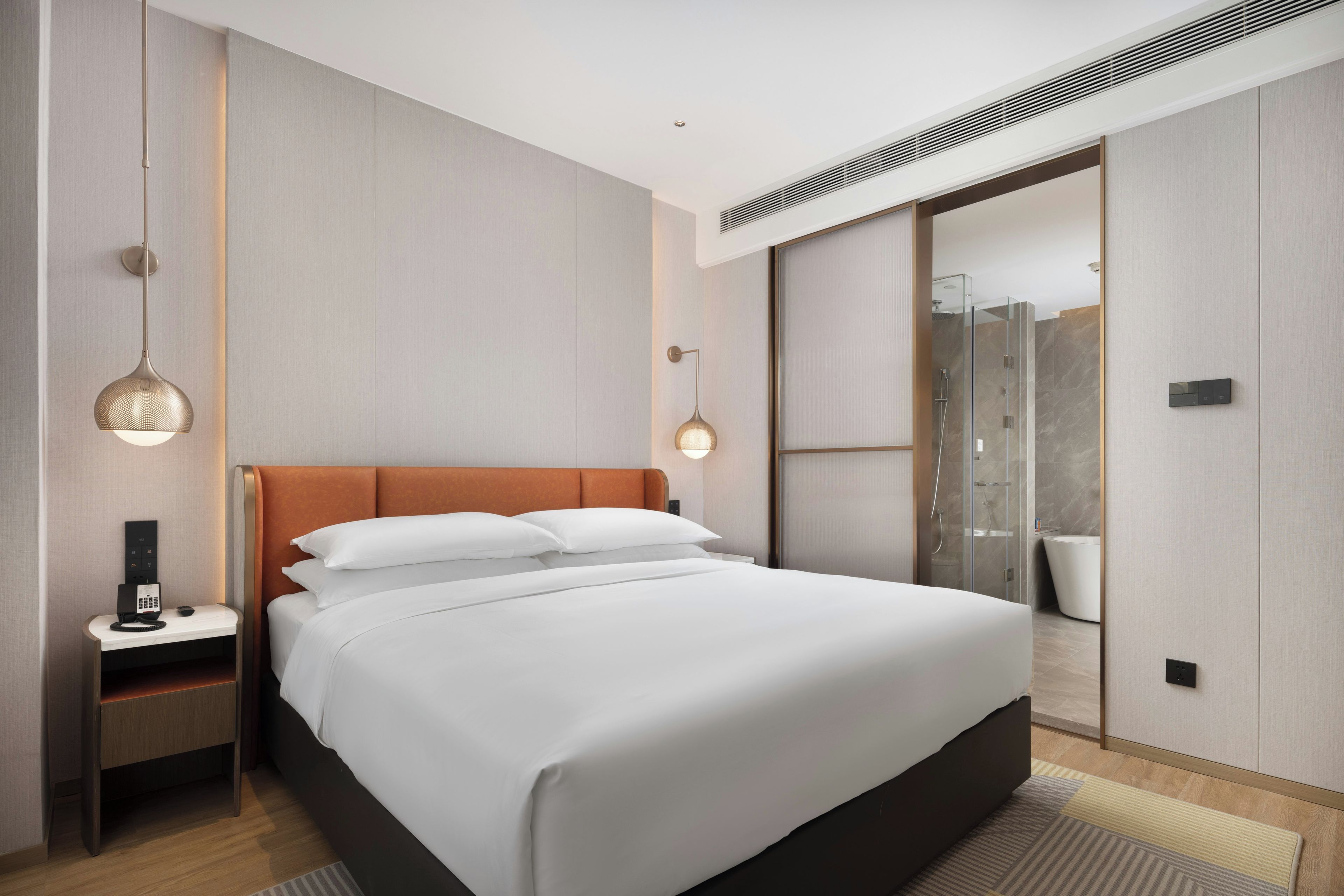 A modern hotel room with a large bed, bedside tables, a desk, and a shower area.