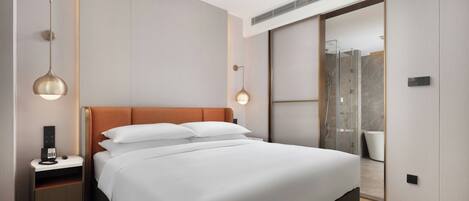 A modern hotel room with a large bed, bedside tables, a desk, and a shower area.