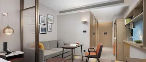 A hotel room with a bed, a sofa, a small table, a chair, a desk with a phone, and a cabinet with a mirror.
