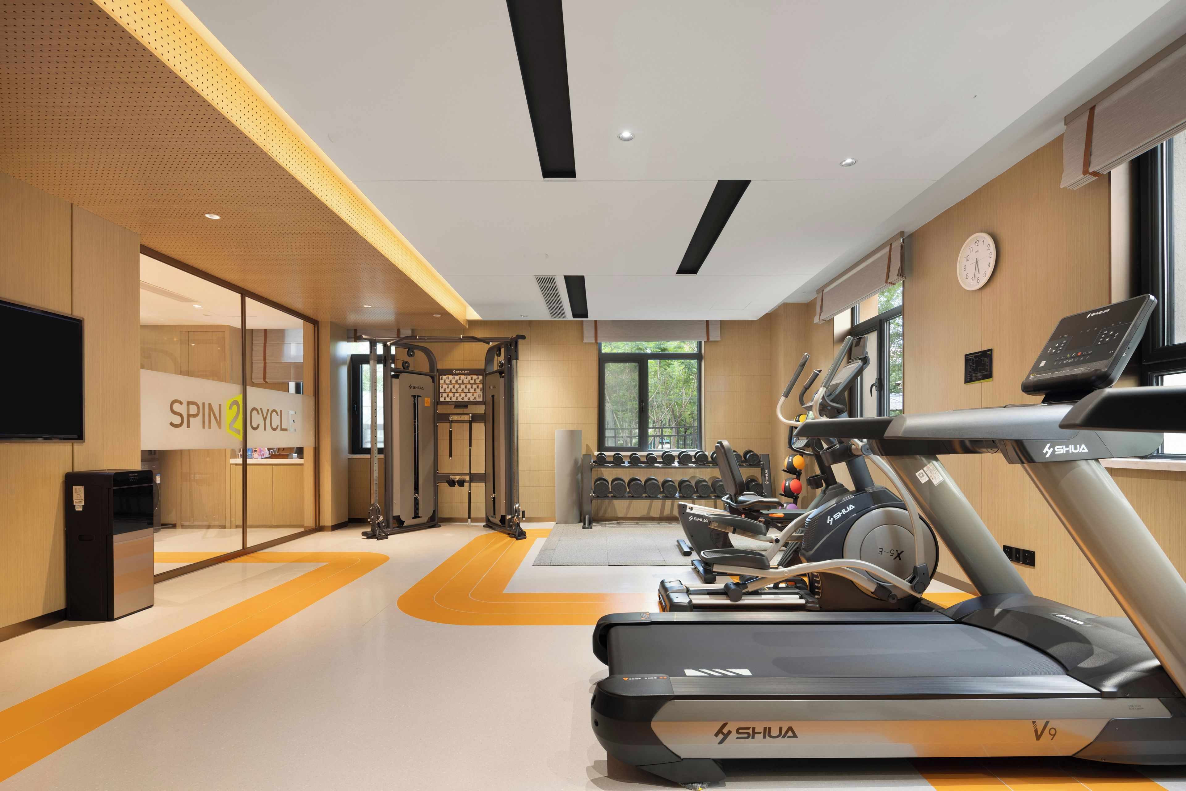 A gym with treadmills, weights, and a wall-mounted clock.