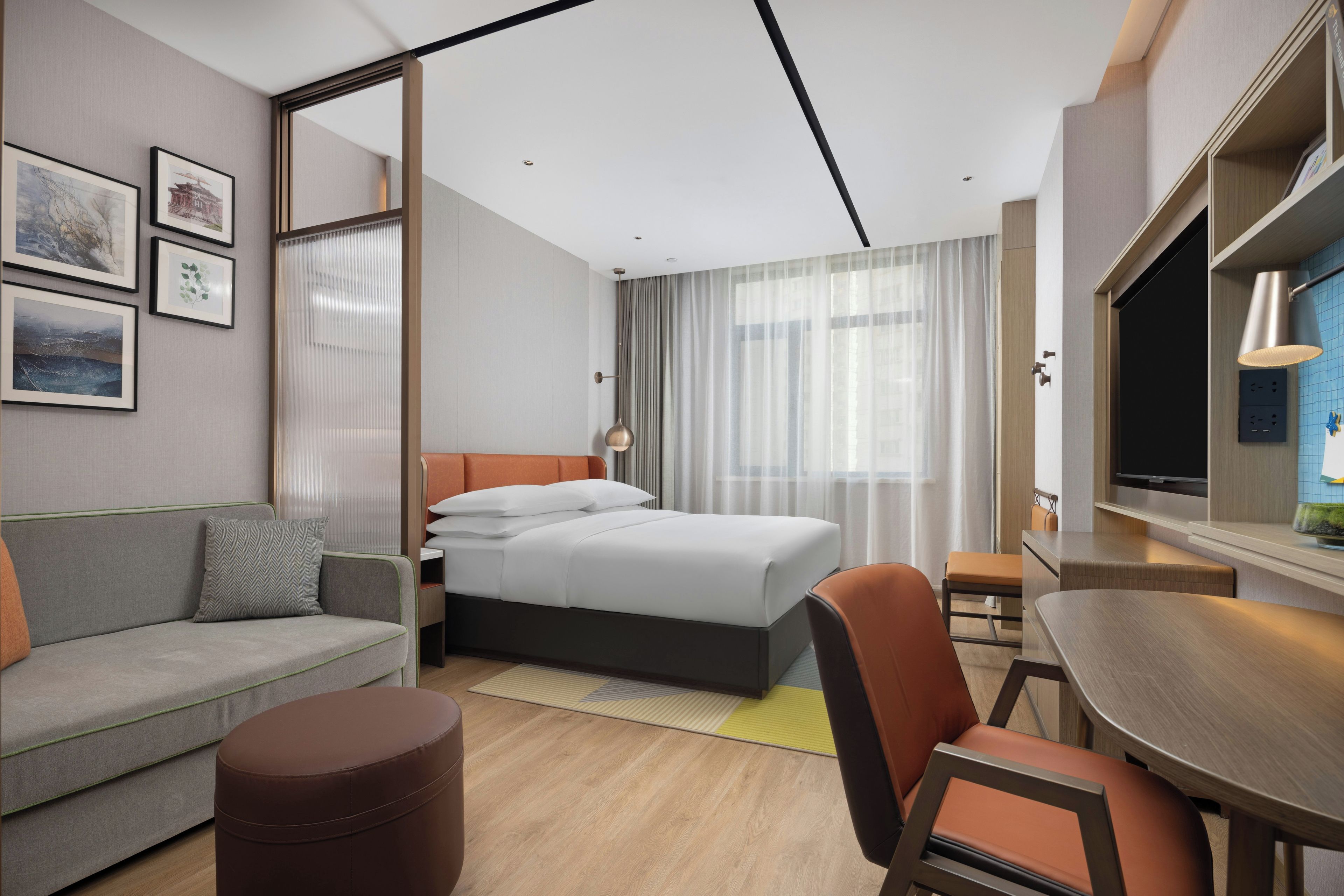 Quarto de hotel moderno com cama, sofá, poltrona e uma pequena mesa.