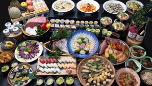 Une variété de plats et d’aliments, notamment des sushis, des sashimis et des fruits de mer, disposés sur une table.