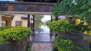 A traditional-style building with a tiled roof, a stone pathway leading to a water feature, and lush greenery.