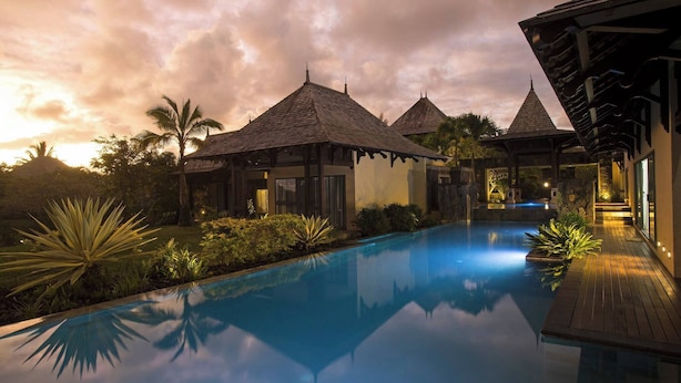 A serene pool area with a clear reflection, surrounded by tropical plants and traditional architecture.