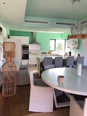 Une cuisine moderne avec des armoires blanches, une hotte en acier inoxydable et un coin repas comprenant une table ronde et des chaises grises.