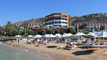 Une plage avec des transats et des parasols, un immeuble à plusieurs étages et une colline en arrière-plan.