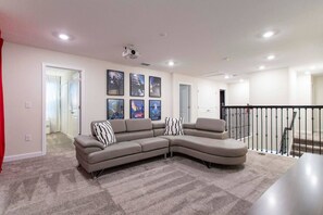 A living room with a sectional sofa, a ceiling-mounted projector, and a staircase with a railing. - South Facing Pool! Private Game Room+Near Disney (Kissimmee)