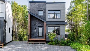 A modern two-story house with a stone facade, a wooden deck, and a gravel driveway. - Le Taiga - Pool Table, Nature, Pet Friendly (Pont-Rouge)