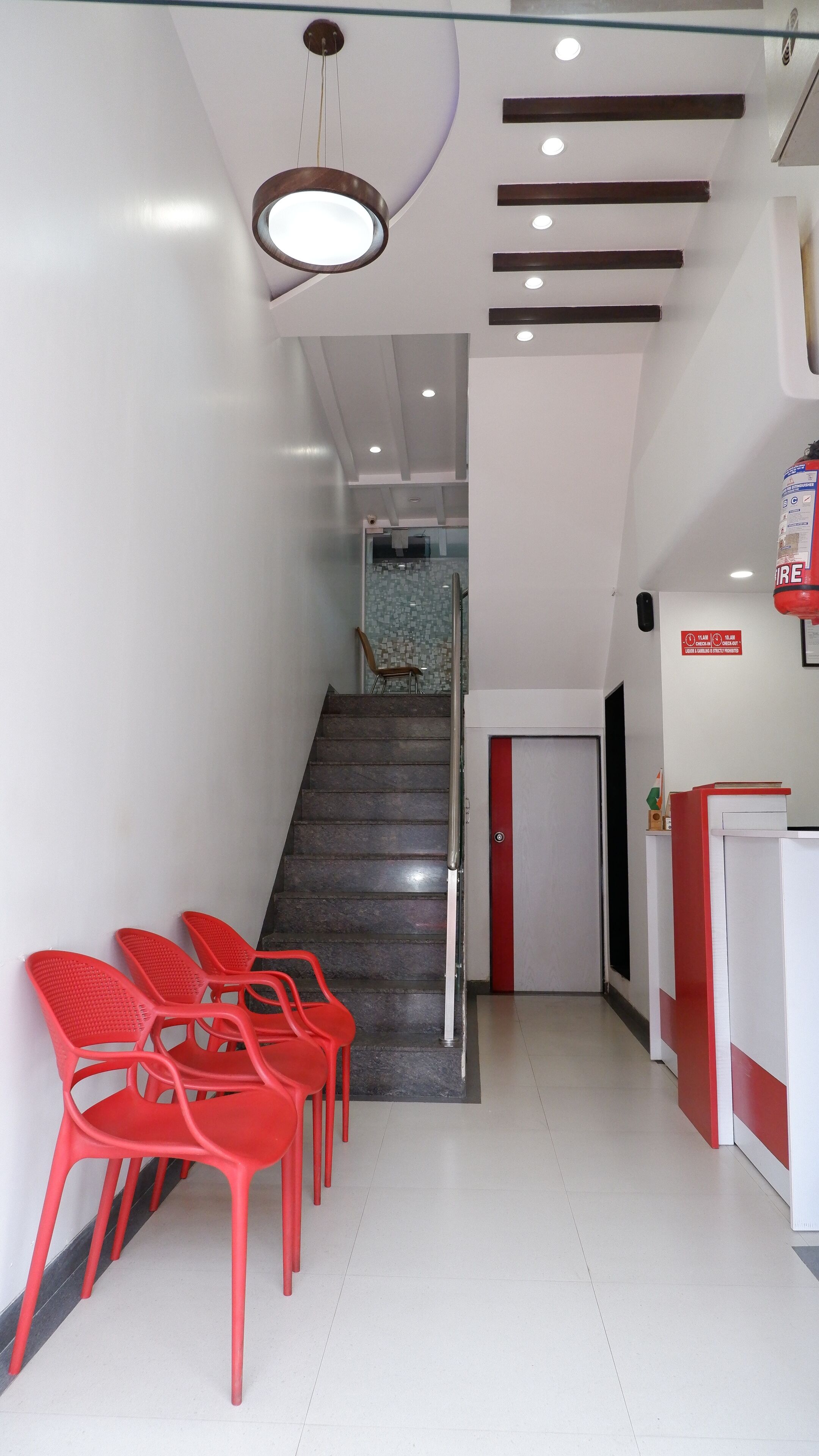 A reception area with a staircase leading to a tiled room. Red plastic chairs are lined up against the wall.