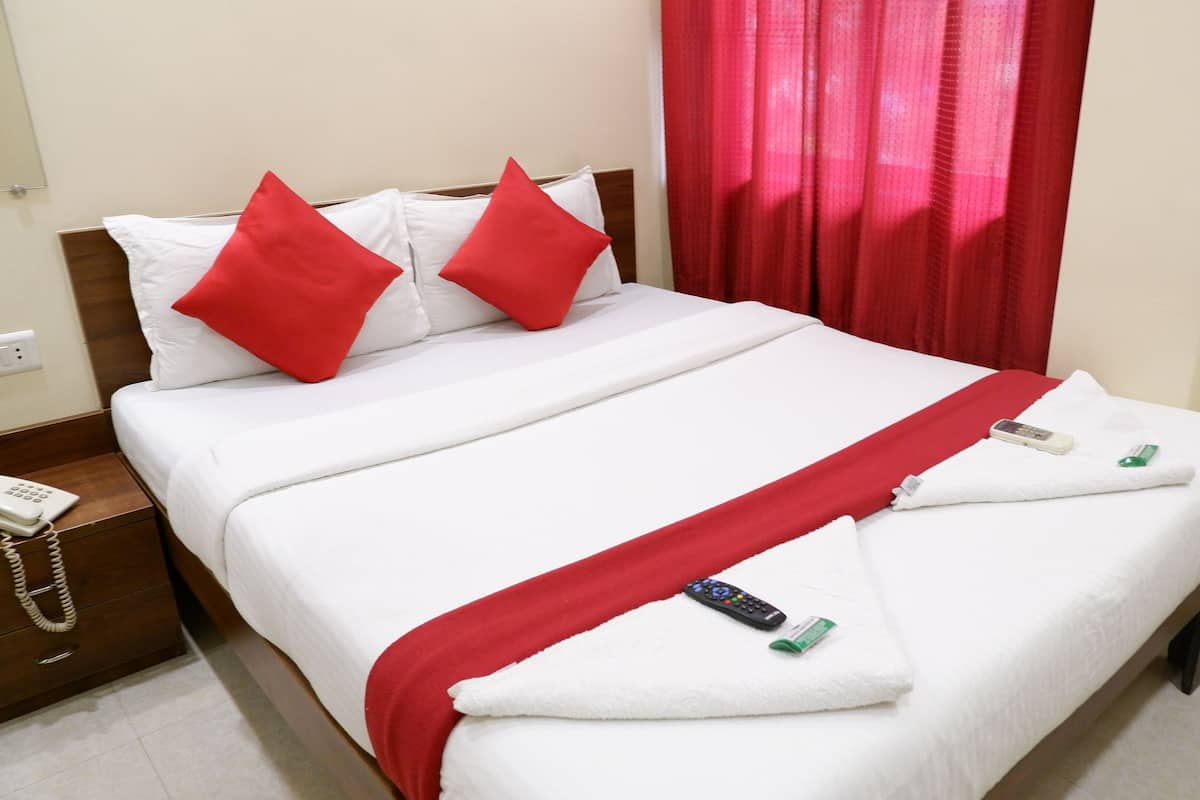 Una cama bien hecha con ropa blanca y almohadas rojas, una manta roja y un control remoto sobre la cama.