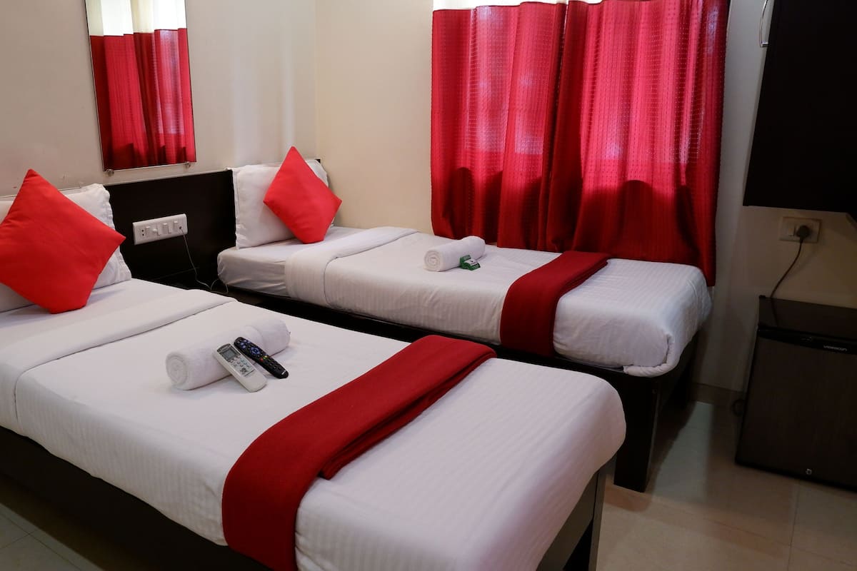 Habitación de hotel con dos camas, cada una con ropa blanca y detalles rojos, televisión y minibar.