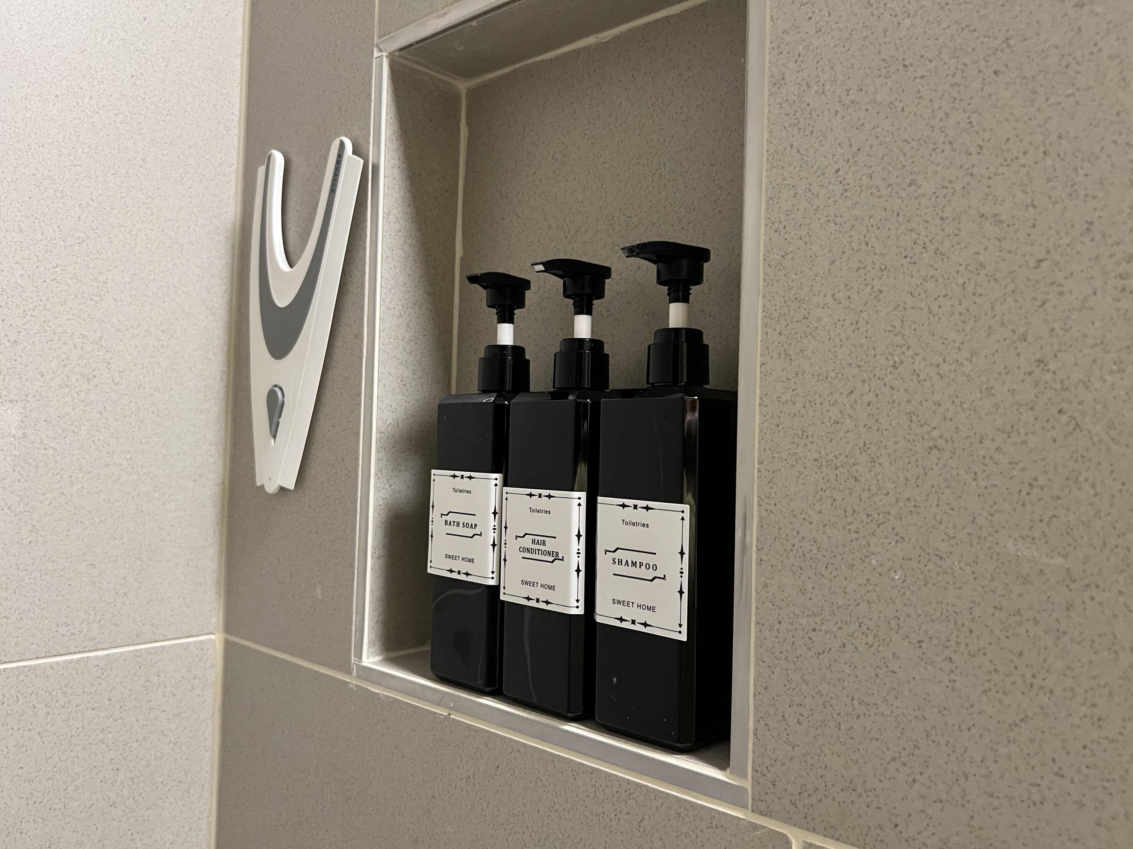 A bathroom with a shelf holding three toiletries bottles labeled 'Bath Soap', 'Hair Conditioner', and 'Shampoo'.