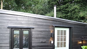 A wooden cabin with a white door, a window with a decorative glass, and a sign that reads "WOODLAND LOOSE". - Charming Woodland Lodge 2 Person 1 Bedroom (Great Yarmouth)
