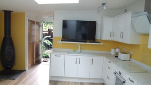 A modern kitchen with white cabinets, a built-in oven, a large flat-screen TV, and a black stove. - Charming Woodland Lodge 2 Person 1 Bedroom (Great Yarmouth)