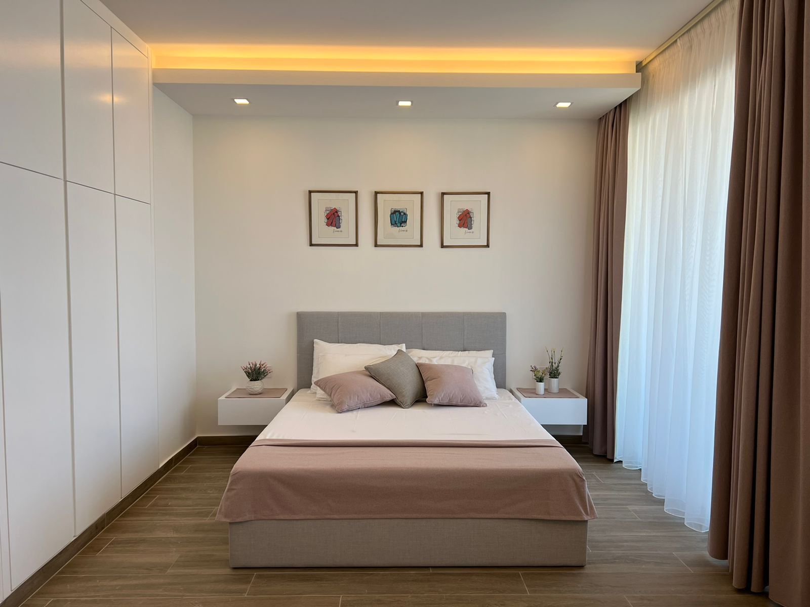 A modern bedroom with a large bed, two bedside tables, and a window with curtains.