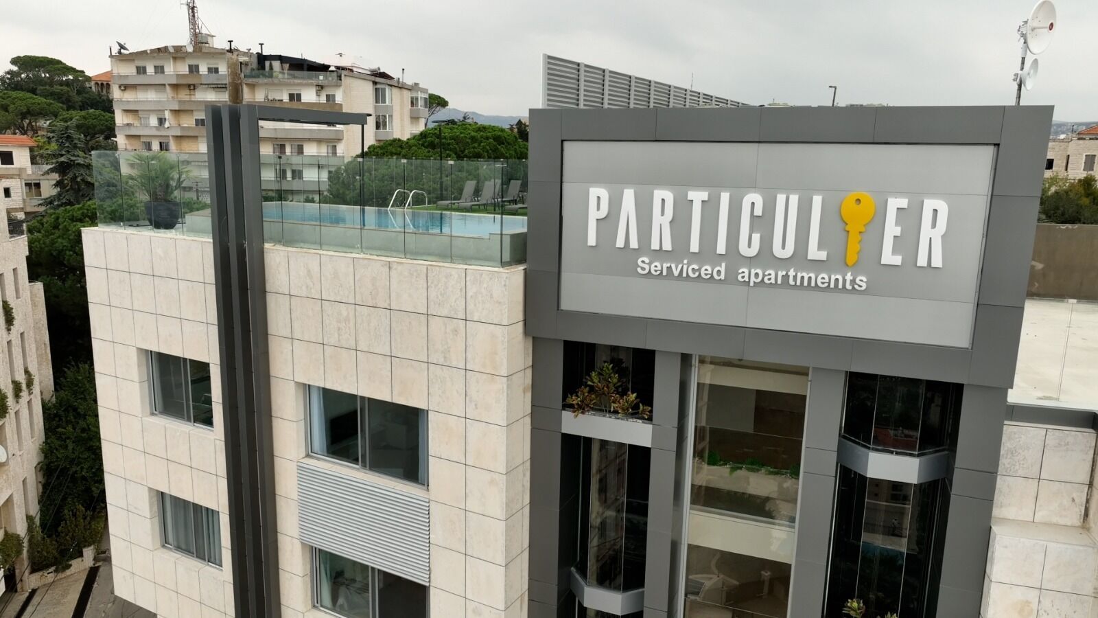 A building with a sign that reads "PARTICULER Serviced apartments" and a pool area visible in the background.
