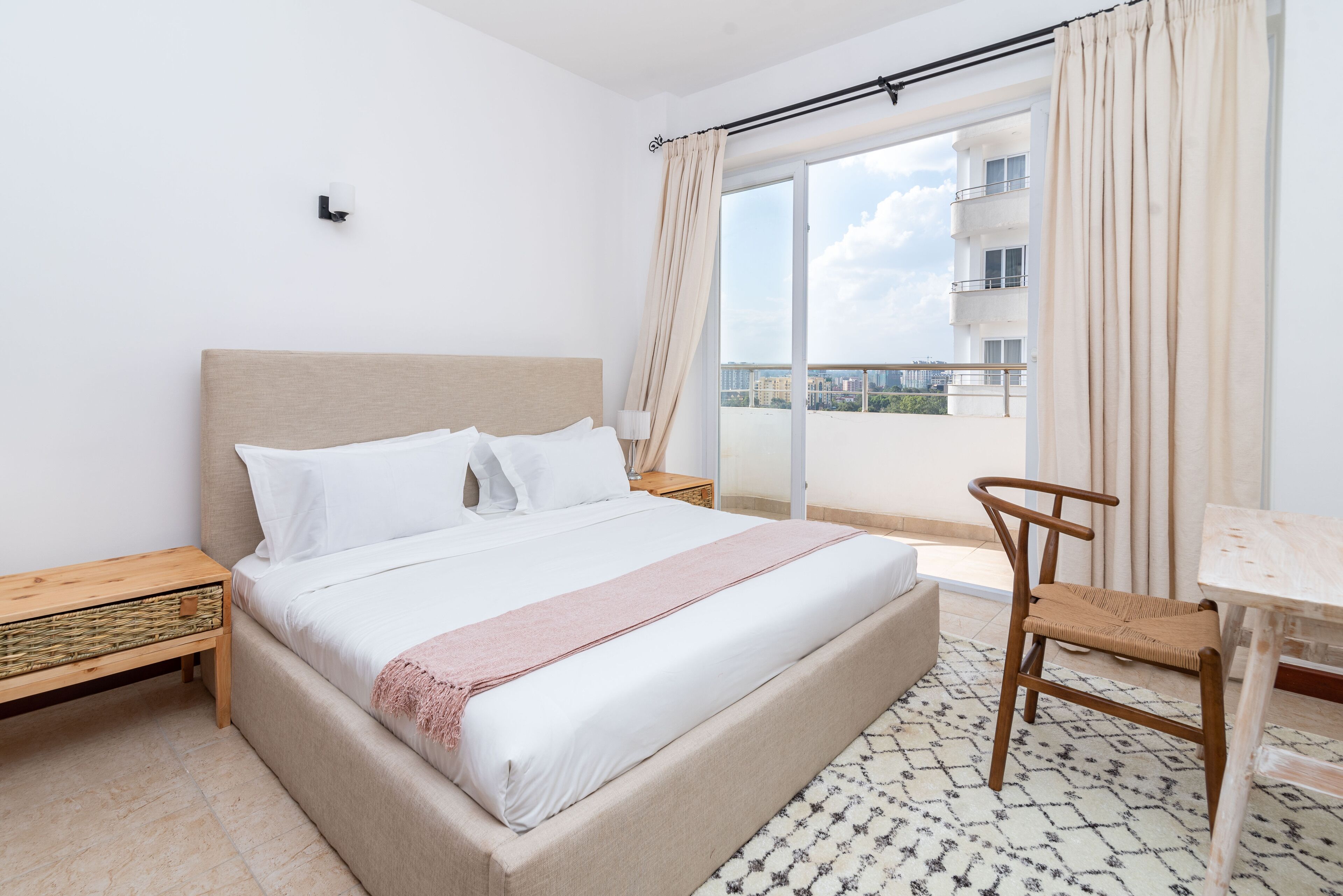 Une chambre à coucher comprenant un lit, une chaise, une petite table, une table de chevet et une vue sur l’extérieur.