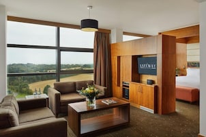 Una habitación de hotel moderna con un ventanal grande, un sofá, una mesa de centro, un televisor y una cama.