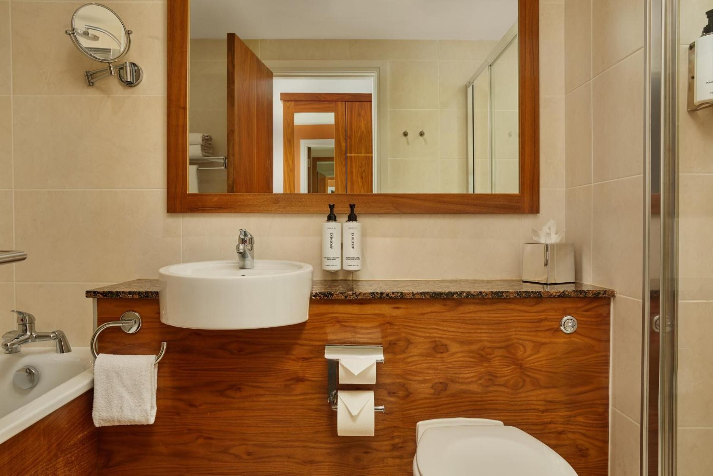 A bathroom with a wooden vanity, a sink, a mirror, a toilet, and a shower.