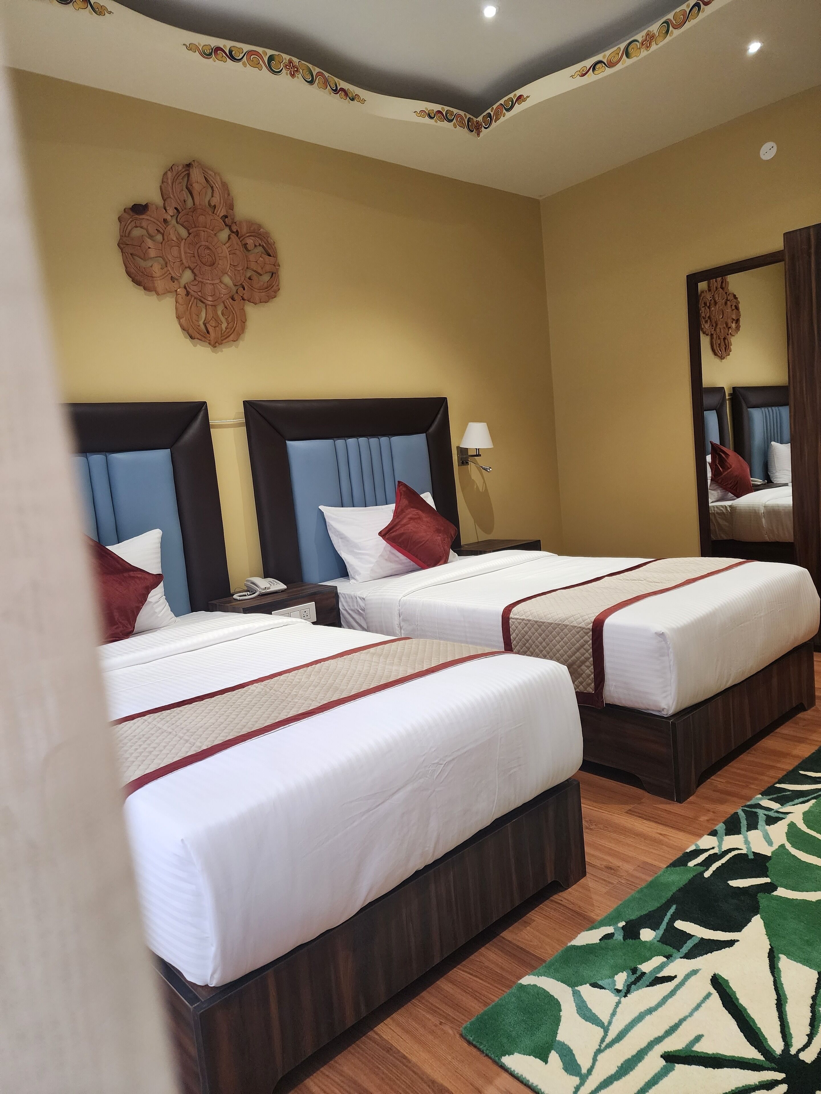 A hotel room with two beds, each with a headboard, a bedside table with a lamp, and a mirror on the wall.